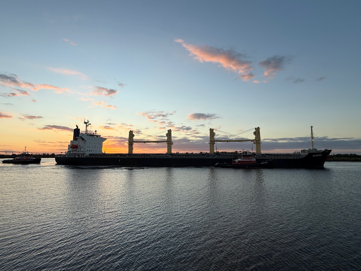 Bulk carrier vessel arriving at Lake Charles port at sunset, assisted by tugboats on calm water — Gulf Coast operations