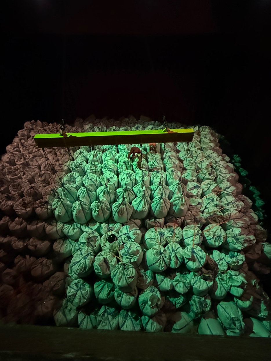 GCS crew discharging supersacks at night — crane spreader bar lit in green over packed bulk bags