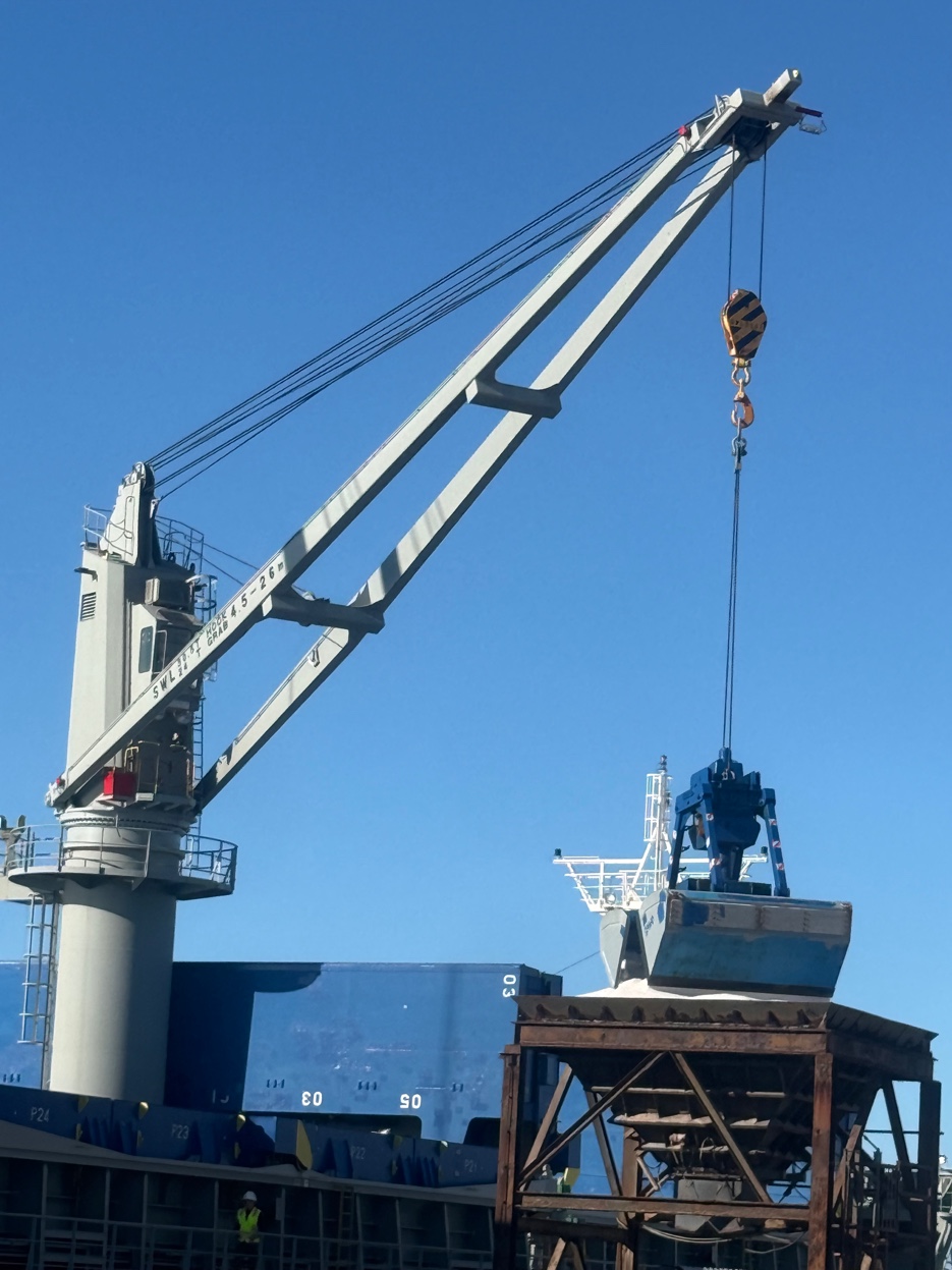 Ship-mounted crane with grab bucket attachment at a Gulf Coast port — clear blue sky