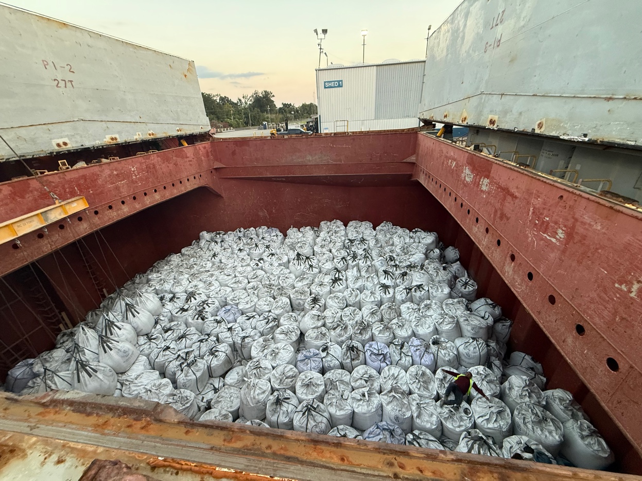 Ship hold packed with rows of bulk bags ready for discharge — dusk sky visible above deck